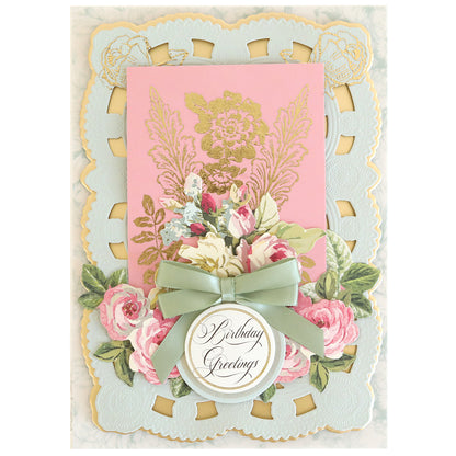 Decorative handmade birthday card created with 3D Layer Dies with Pre-Tied Bows, featuring scalloped edges, gold floral detailing, pink and white flowers, satin bows, a green ribbon, and a round tag that reads “Birthday Greetings”—all enhanced for added dimension.
