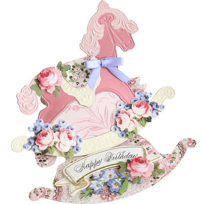 Celebrate baby milestones or holidays with a decorative birthday card made using Rocking Horse 3D Dies—pink rocking horse shape, floral patterns, 3D flowers, blue bow, and "Happy Birthday" message. Perfect for creative crafting!.