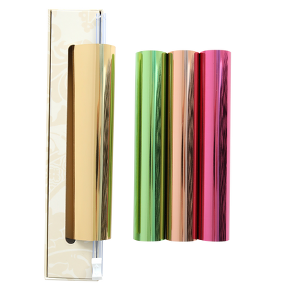 Four metallic foil rolls in shiny gold, green, orange, and pink stand upright next to a box with a sliding cutter on a white background. The Perfect Palette Antique Gild Hot Foil set is perfect for adding eye-catching accents to your crafts, just like those created with the Anna Griffin Gild Hot Foil system.