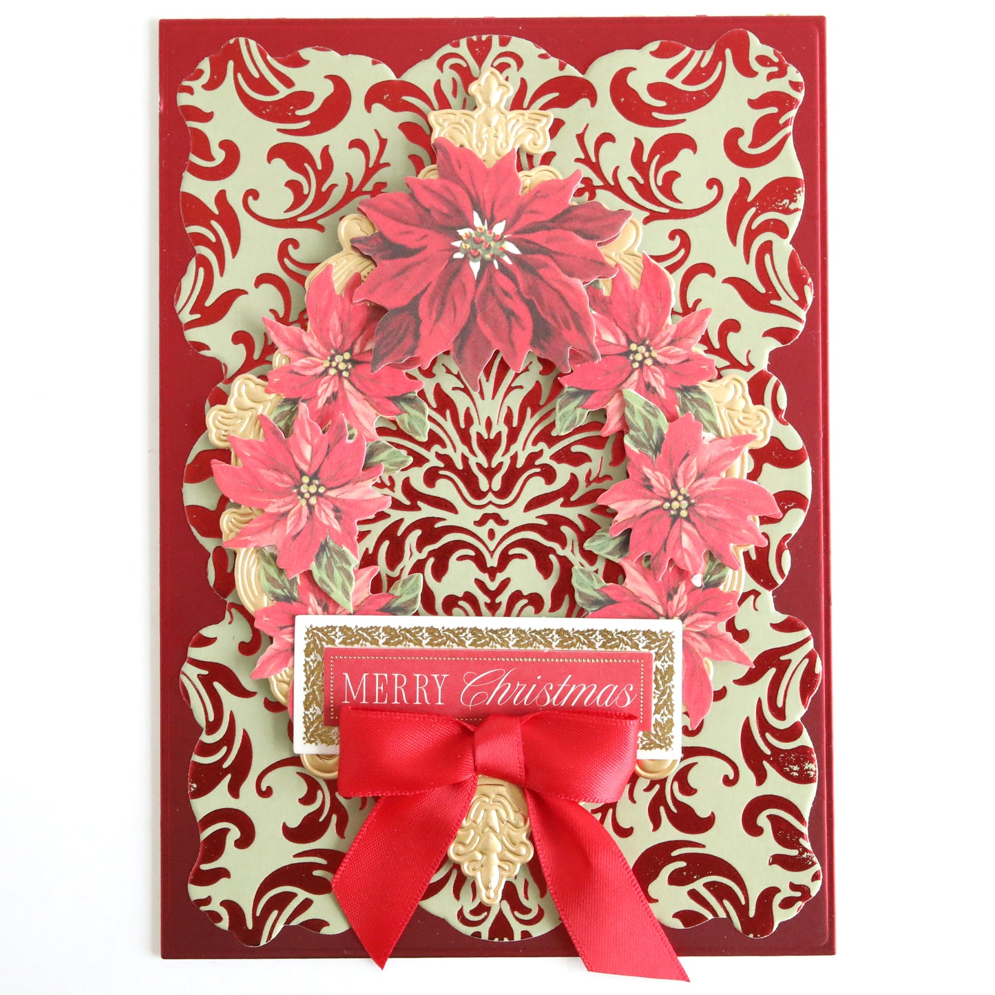 A Christmas card created with the Empress Gild Hot Foil Machine and Holiday Hot Foil features a luxurious red and gold damask pattern, a wreath of red poinsettias, a red ribbon bow, and an elegant "Merry Christmas" label.