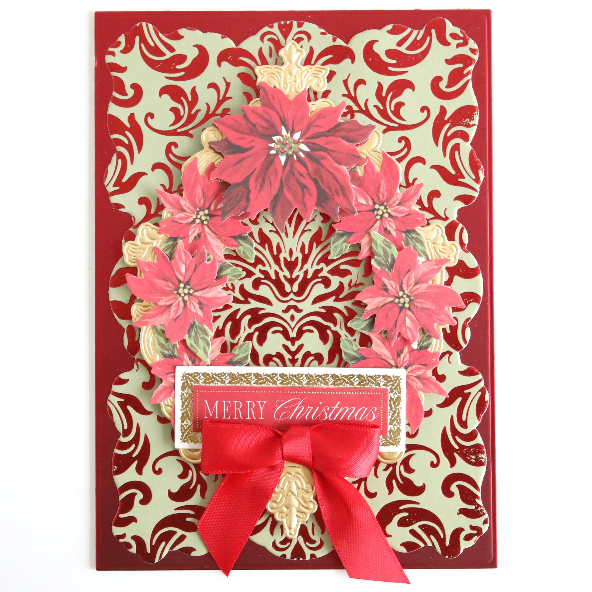 A Christmas card created with the Empress Gild Hot Foil Machine and Holiday Hot Foil features a luxurious red and gold damask pattern, a wreath of red poinsettias, a red ribbon bow, and an elegant "Merry Christmas" label.