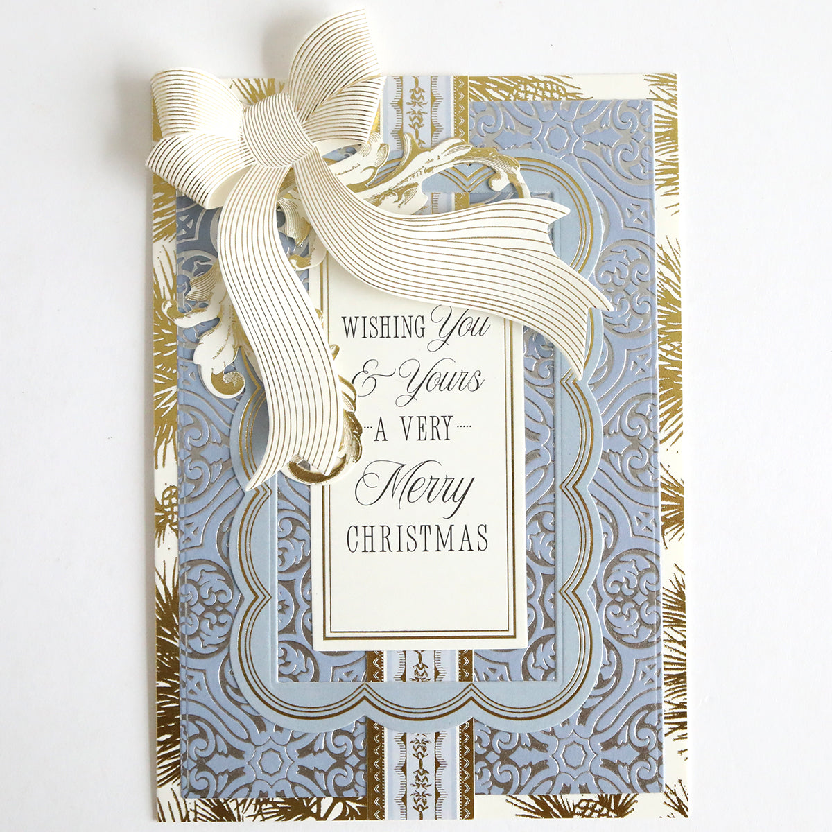 A holiday card, created with the Empress Gild Hot Foil Machine and Holiday Hot Foil, features a cream ribbon and an ornate blue and gold design with the message, "Wishing you & yours a very Merry Christmas.