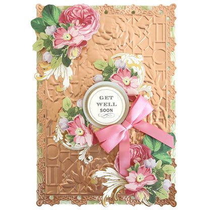 A rectangular greeting card created with Garden Gate and Pavilion 3D Embossing Folders, featuring a copper geometric background, pink flowers, a pink ribbon, and a “Get Well Soon” circular tag.