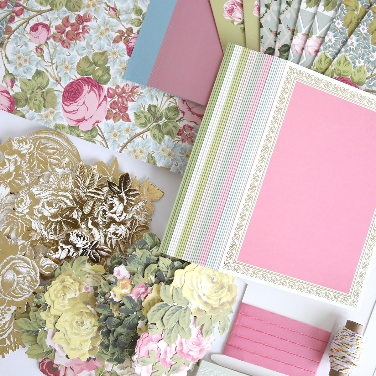 The Rose Ultimate Paper Crafting Collection includes floral papers, ornate gold cutouts, bordered blank cards, and decorative ribbon arranged for creative scrapbooking.