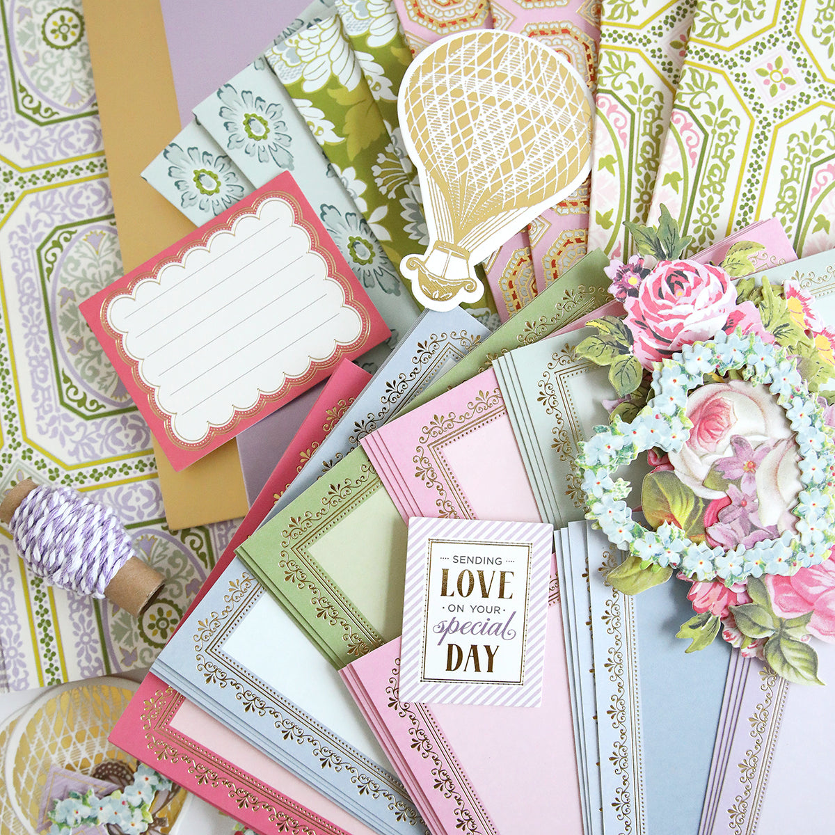 The Charlie Ultimate Paper Crafting Collection features assorted decorative stationery, envelopes, and cards with floral, balloon, and ornate patterns, plus twine, embellishments, and a card that says "Sending love on your special day.