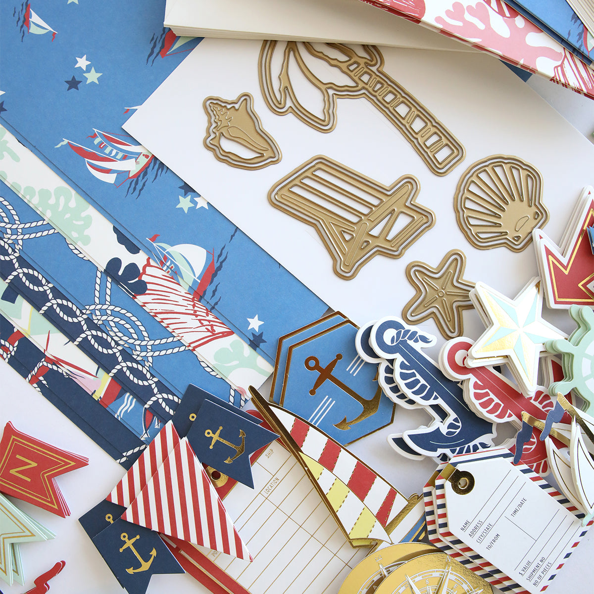 A variety of nautical-themed paper crafts—such as decorative cutouts, patterned sheets, anchor and shell shapes, and colorful tags—are arranged on a flat surface, ideal for use with the Seafarer Papercrafting Kit with Dies.
