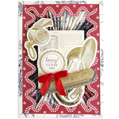 The Patriotic Papercrafting Kit with Dies includes black-and-white straws, vintage kitchen utensil die-cuts, a “Hooray! It’s your day!” badge, and a red ribbon—perfect for Americana fans—set on a bold red patterned background.