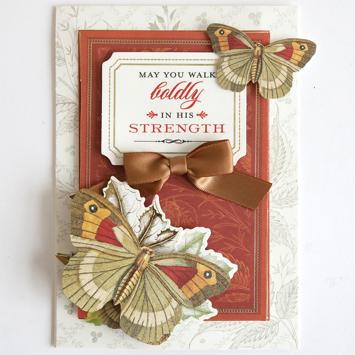 Send heartfelt support with the Prayer Sentiment Rub On Transfers, featuring layered butterflies, a brown ribbon bow, and the inspiring message "May you walk boldly in His strength" on a red and white background.