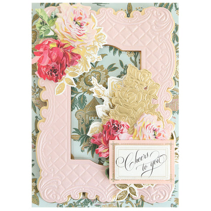 Greeting card featuring a pink embossed frame made with the Tufted Rose Concentric Frames 3D Die Set, adorned with floral accents and a "Cheers to you" label on a patterned background.