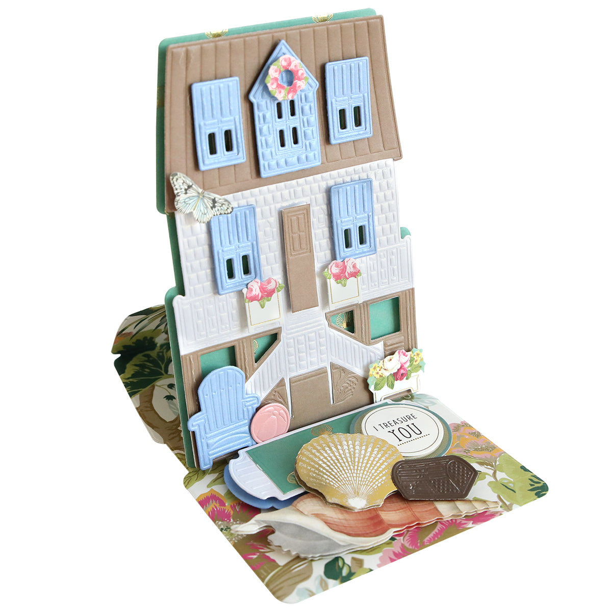 The Summer House 3D Easel Dies create a decorative beach cottage card with blue shutters, flowers, and beach accents on a floral base—ideal for summer crafting and making charming three-dimensional house cards.