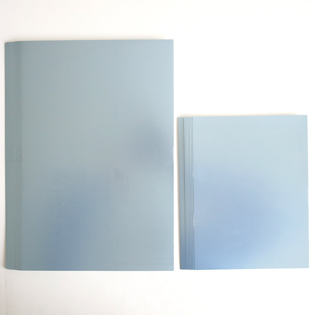 Two stacks of Luxury Hydrangea Blue Matte Foil Cardstock, one large and one small, are placed side by side on a white background. The sheets have a translucent blue appearance similar to blue cardstock.