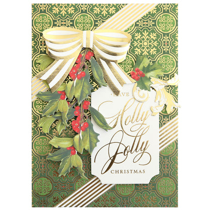 Craft a festive card with the Christmas Grace Card Making Kit, showcasing gold and green designs, a gold striped ribbon bow, holly leaves and red berries, plus a “Have a Jolly Jolly Christmas” tag.
