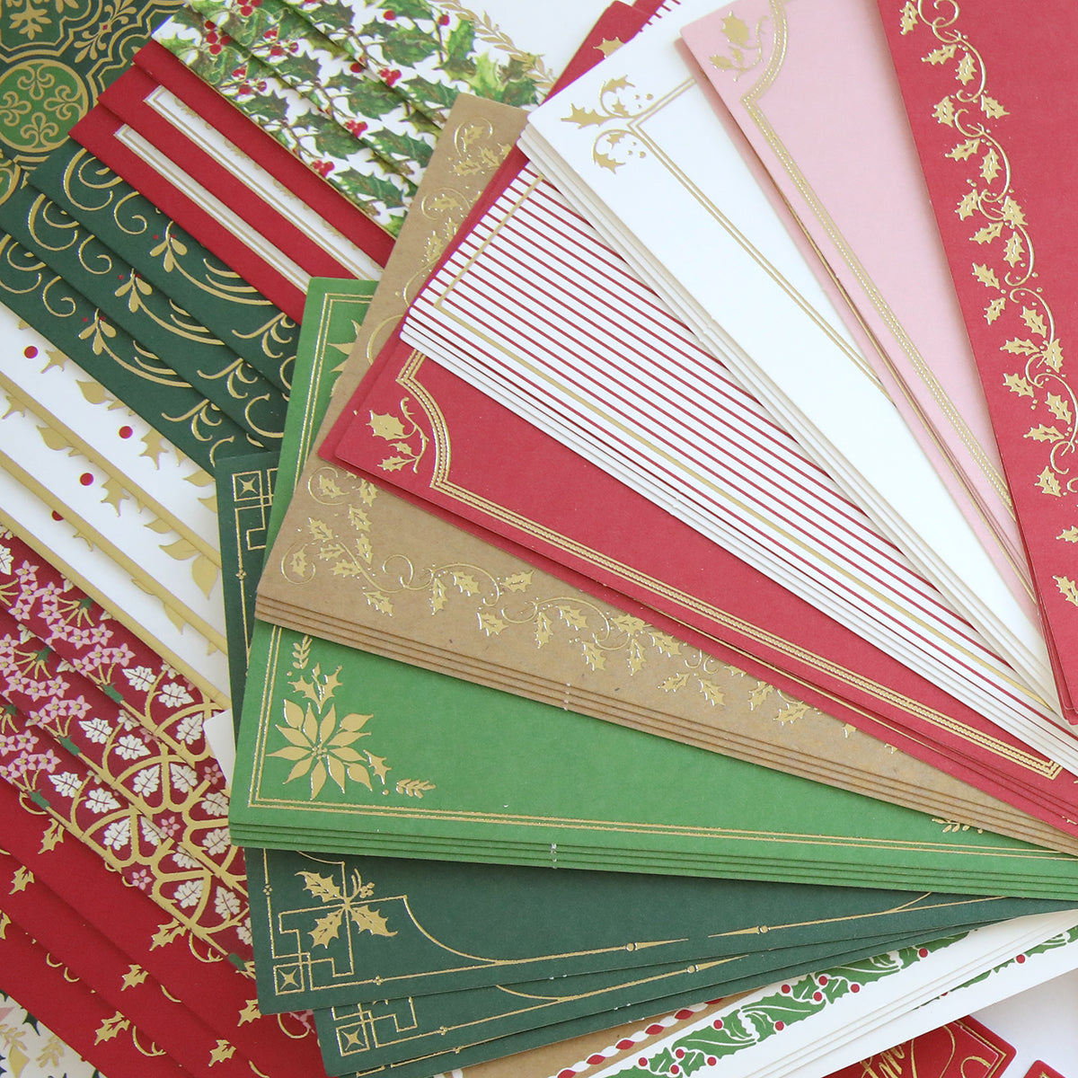 The Christmas Grace Card Making Kit features colorful envelopes and handmade Christmas cards with festive red, green, white, and gold holiday designs.