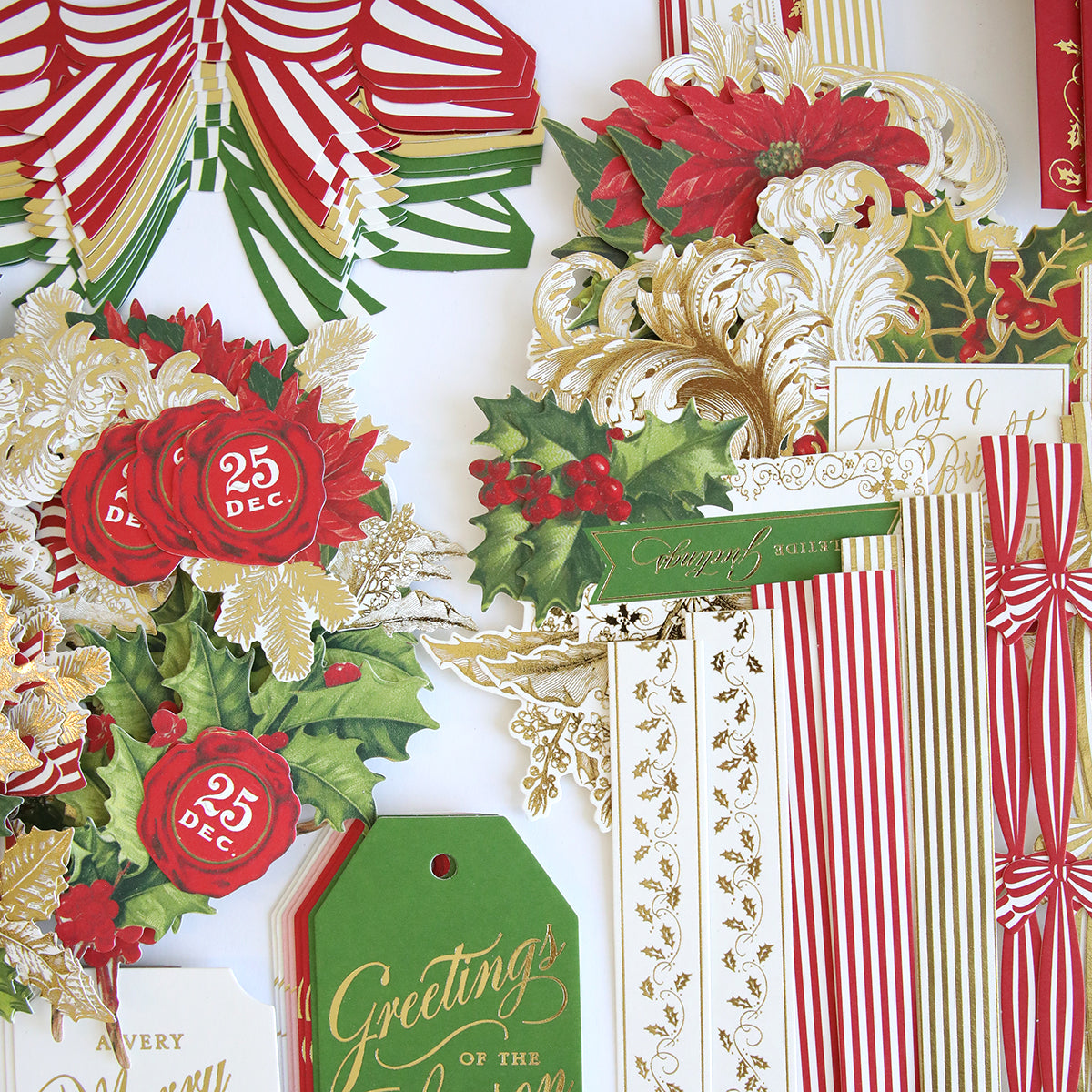 The Christmas Grace Card Making Kit includes assorted holiday paper decorations with floral designs, holly leaves, gold accents, and festive tags—featuring “25 Dec” and “Greetings” in red, green, and gold—perfect for handmade Christmas cards.