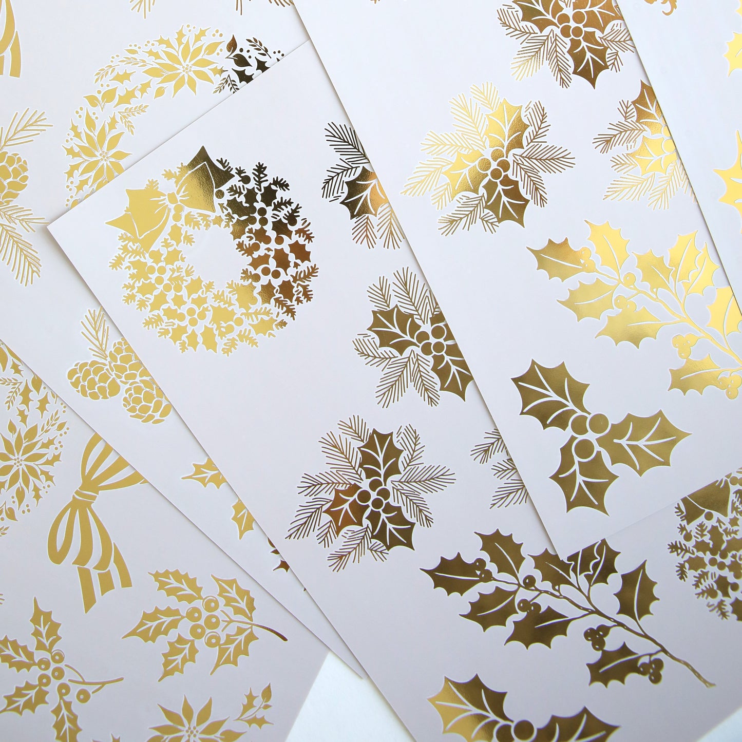 Holiday Nostalgia Foil Rub Ons feature white sheets with gold foil Christmas designs—holly, berries, wreaths, and bows—in an overlapping layout, ideal for adding vintage shimmer to your festive papercrafting projects.