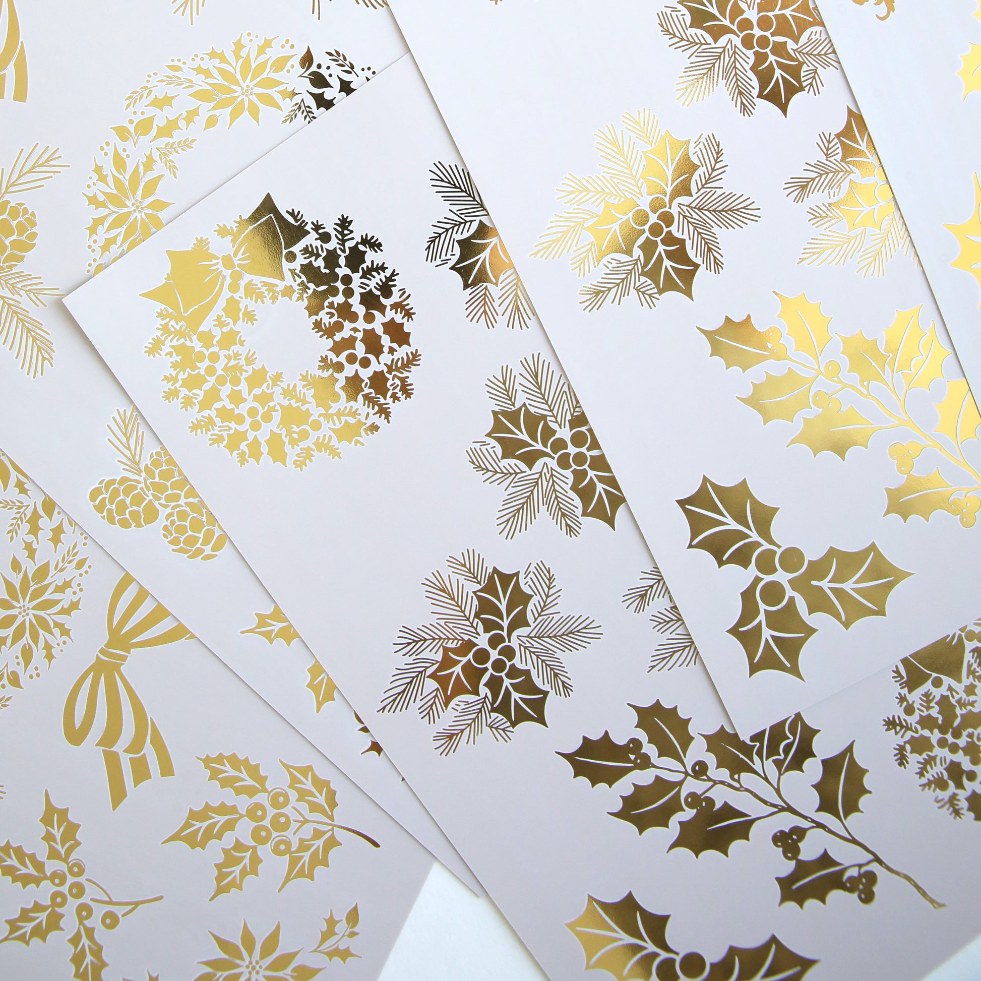 Holiday Nostalgia Foil Rub Ons feature white sheets with gold foil Christmas designs—holly, berries, wreaths, and bows—in an overlapping layout, ideal for adding vintage shimmer to your festive papercrafting projects.