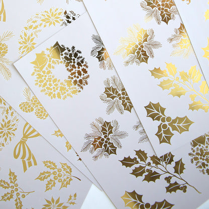 Holiday Nostalgia Foil Rub Ons feature white sheets with gold foil Christmas designs—holly, berries, wreaths, and bows—in an overlapping layout, ideal for adding vintage shimmer to your festive papercrafting projects.
