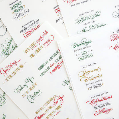 Christmas Card Sentiment Rub Ons—assorted sheets featuring festive Christmas greetings in various fonts and colors like red, green, gold, and black, overlapping on a white background; ideal for embellishing handmade cards or adding to holiday paper crafts.