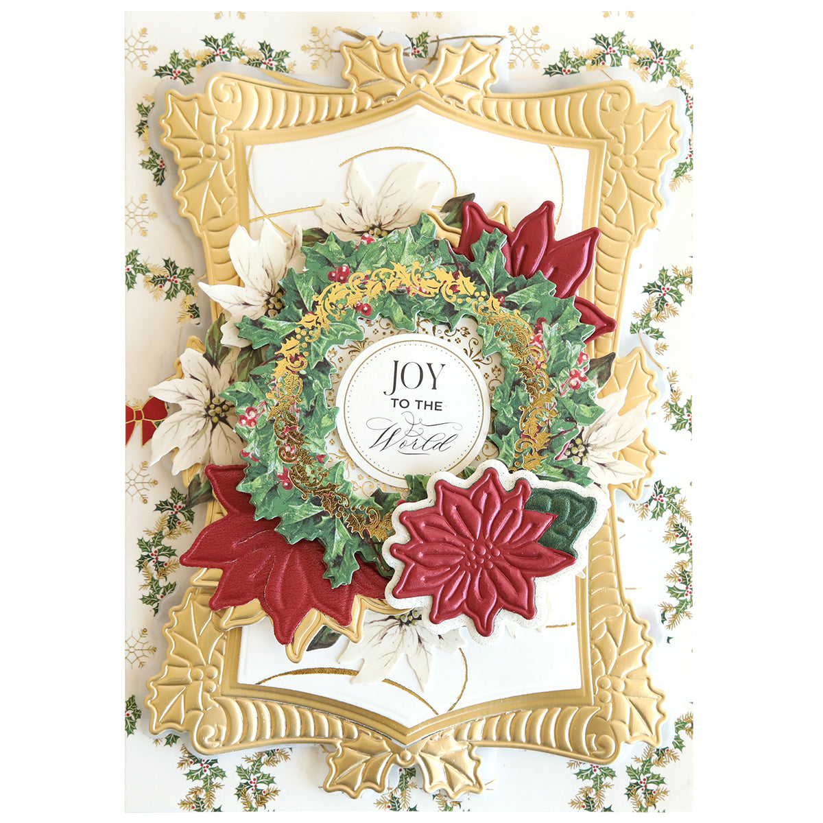 A decorative holiday card showcases a gold frame, white poinsettias made with the Poinsetta Scroll Frame 3D Dies, red leaves, and a wreath displaying "Joy to the World" in the center.