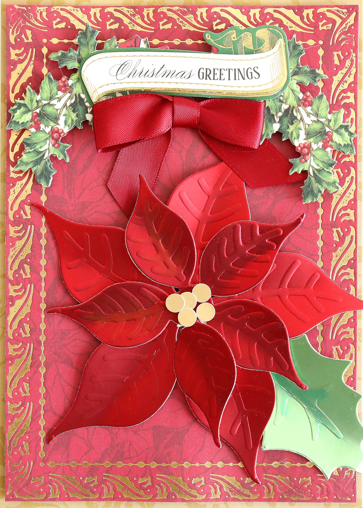 A Christmas card featuring red and gold borders, a vibrant red poinsettia, holly leaves, and a "Christmas Greetings" banner topped with a red ribbon bow—ideal for Christmas card making when crafted with Holiday Color Drenched Cardstock to enhance its vibrancy and elegance.