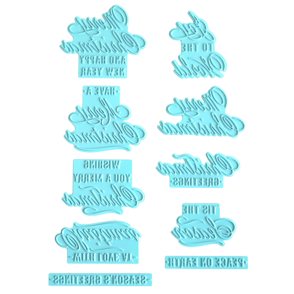 Eight blue plastic embossers with reversed festive phrases, such as "Happy New Year," "Season's Greetings," and "Wishing You A Merry Christmas," are arranged on a white background. These embossers are ideal for adding charming holiday greetings to your foiled Christmas cards or for use with the Gilded Small Christmas Sentiments Hot Foil Plates.