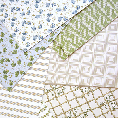The Jack Cardstock Collection showcases sheets of 12x12 pastel cardstock with blue florals, green leaves, geometric squares, stripes, and lattice designs that overlap for an elegant scrapbook display.
