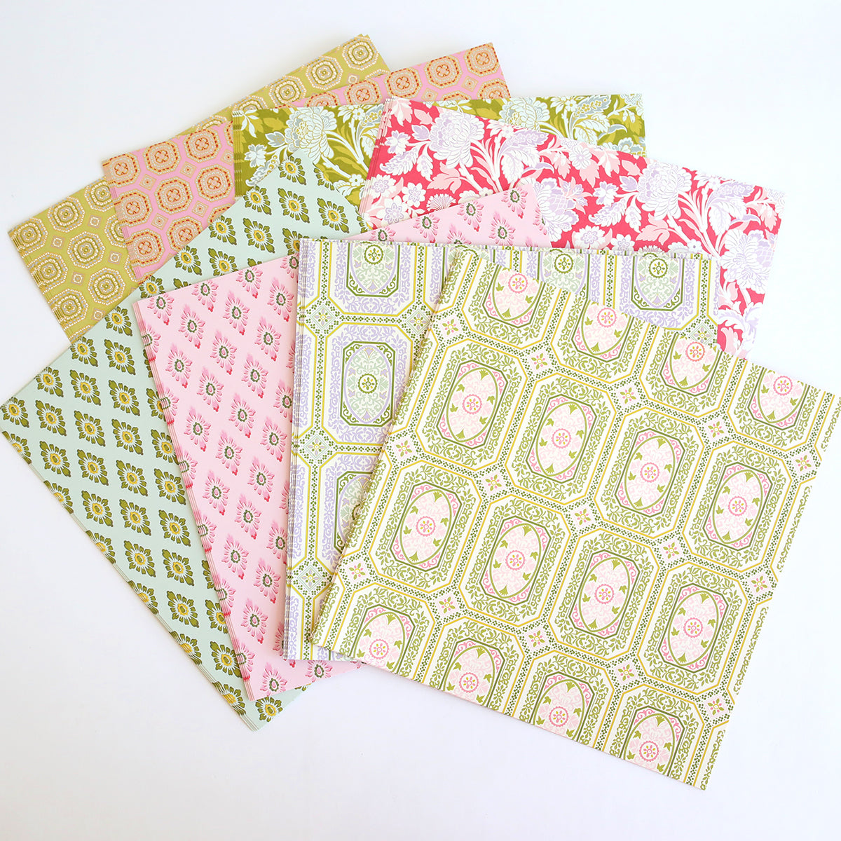 Seven sheets from the Charlie Double Sided 12x12 Cardstock Collection in pink, green, and white are arranged in a fan shape on a white background. Each sheet features a unique geometric or floral pattern, making them perfect for layered paper crafts.