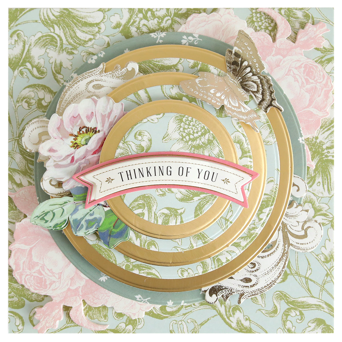 A decorative card featuring gold concentric circles created with the Concentric Shape Dies Bundle (all 4 sets), floral designs, a butterfly, and a "Thinking of You" banner on a pastel patterned background.