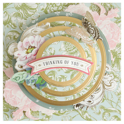 A decorative card featuring gold concentric circles created with the Concentric Shape Dies Bundle (all 4 sets), floral designs, a butterfly, and a "Thinking of You" banner on a pastel patterned background.