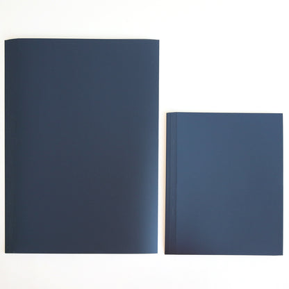Two closed notebooks from the Celebration Foil Cardstock Collection, one larger and one smaller, in a dark blue shade are placed side by side on a plain white surface. Their sturdy covers resemble navy matte foil cardstock, making them perfect for stylish journaling or as inspiration for elegant paper crafts.