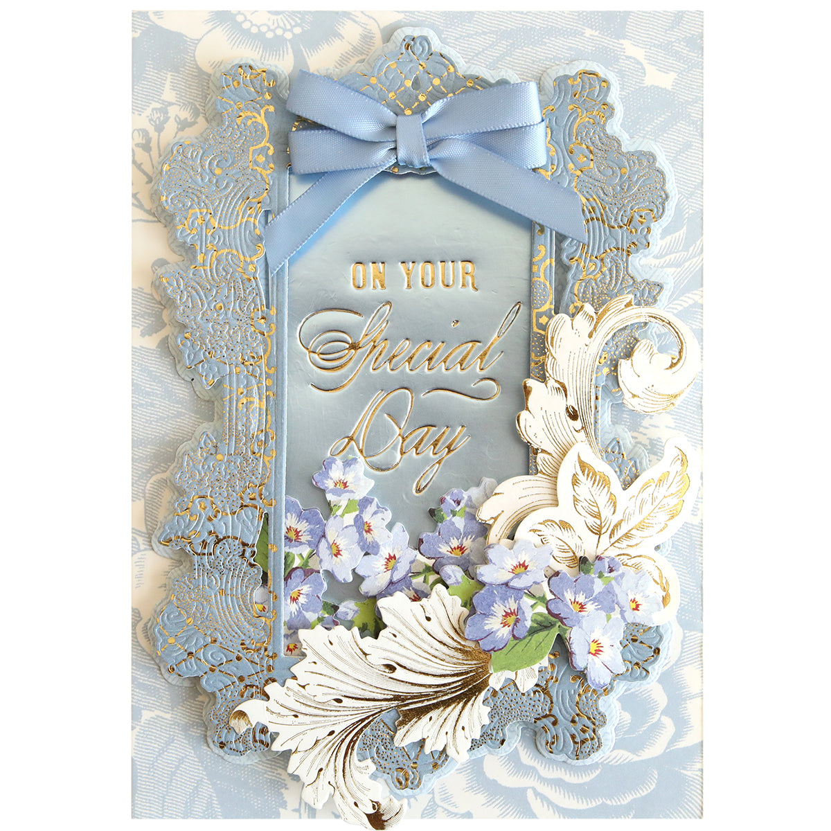 A decorative card featuring “On Your Special Day” in gold script, adorned with blue and white flowers, ornate borders, and a blue ribbon bow at the top against a floral-patterned background—perfect for conveying heartfelt birthday wishes. The elegant design is beautifully enhanced using the Set of 30 Gilded Small Sentiment Plates for an added touch of charm.