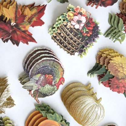Fall Ephemera Embellishments featuring an assortment of autumn-themed paper cutouts—leaves, a turkey, pumpkins, flowers, and a wicker basket—arranged on a white surface; perfect for Thanksgiving cards and seasonal paper crafting.