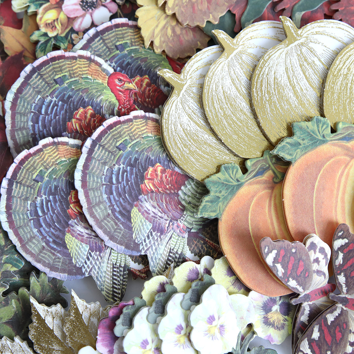 Fall Ephemera Embellishments featuring an assortment of autumn-themed paper cutouts—including turkeys, pumpkins, leaves, flowers, and butterflies—closely arranged for creating Thanksgiving cards and seasonal paper crafting projects.