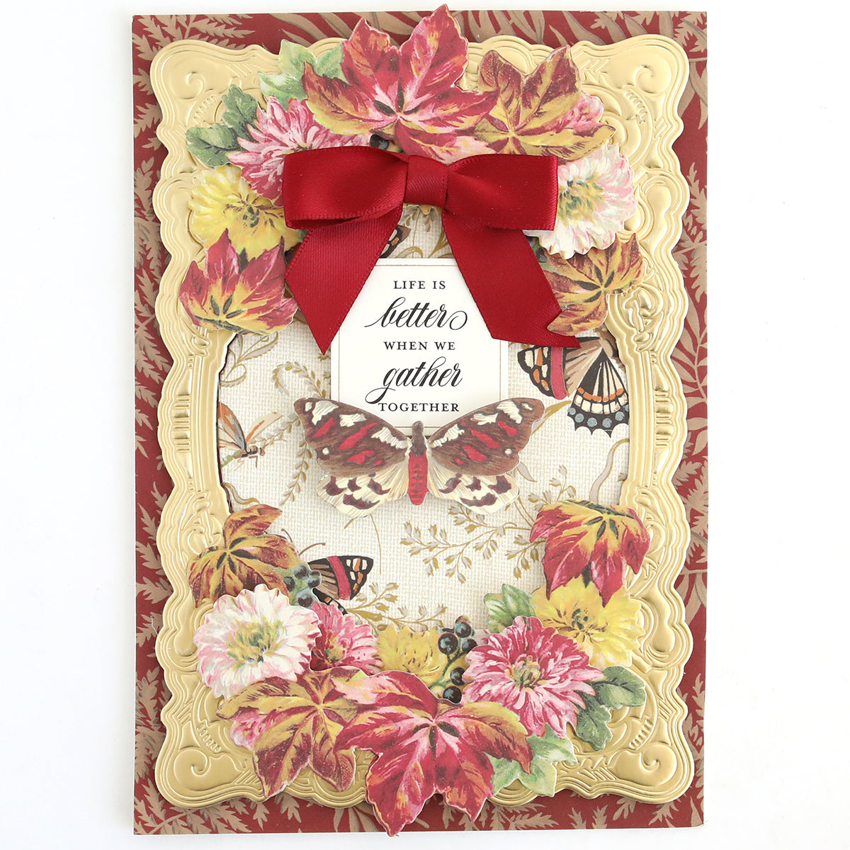 The Fall Ephemera Embellishments feature a greeting card adorned with an embossed gold frame, red bow, autumn leaves, flowers, butterflies, and the heartfelt message “Life is better when we gather together” at the center. Ideal for Thanksgiving cards or seasonal paper crafting projects, these beautiful embellishments capture the warmth and charm of autumn gatherings.
