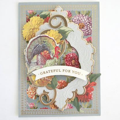 The Fall Ephemera Embellishments set includes a vibrant greeting card featuring a colorful turkey illustration, floral background, ornate white and gold frame, and a “Grateful For You” banner. Ideal for autumn scrapbooking, this set offers charming Thanksgiving touches to enhance your heartfelt creations.