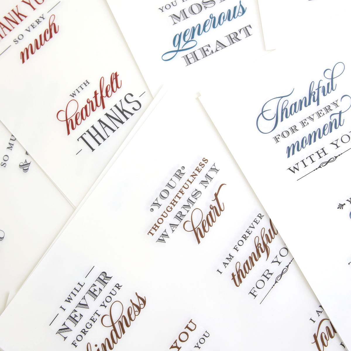 A collection of white cards adorned with elegant, cursive thank you messages in black, blue, and red ink—each featuring heartfelt sentiments from the With Gratitude Sentiment Rub Ons—arranged in an overlapping display on a flat surface.