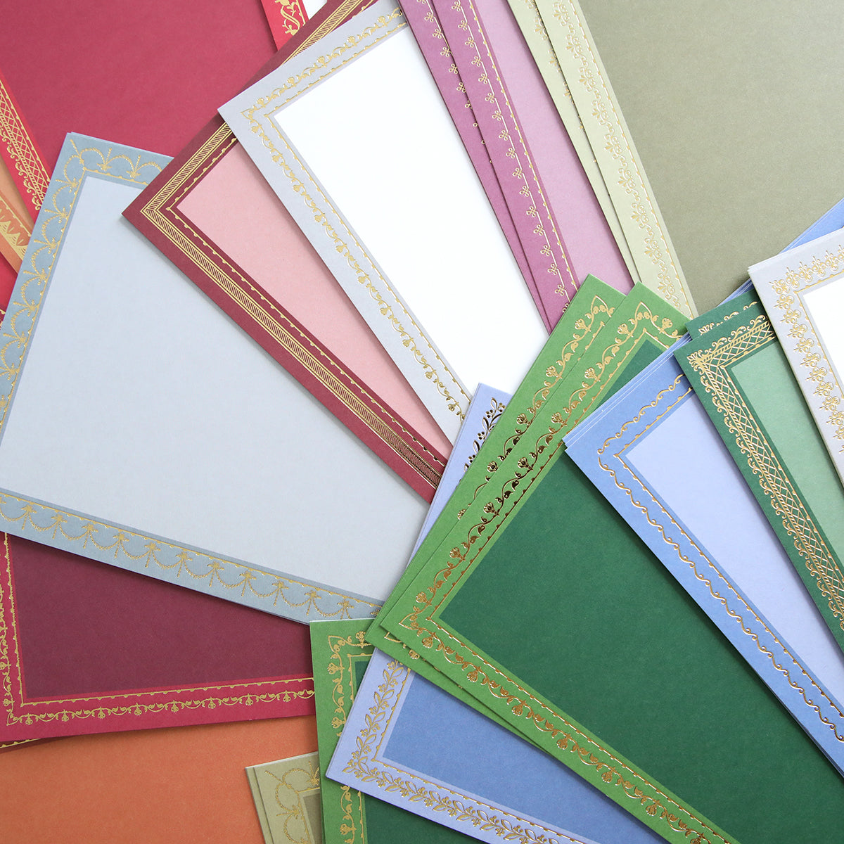 A selection of decorative sheets from the Holiday Photo Mat and Card Layer Bundle, featuring vibrant colors accented with gold-patterned borders, are fanned out on a flat surface—ideal for card making or adding a unique touch as a photo mat card layer.
