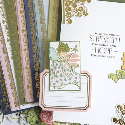 Featuring enchanting fairy artwork, the Dahlia Ultimate Papercrafting Collection includes notecards adorned with fairies, layered over beautifully patterned papers and a white card inscribed in gold and black with the message “Wishing you strength for today and hope for tomorrow,” making this collection ideal for creating handmade cards or bringing a magical touch to scrapbook projects.