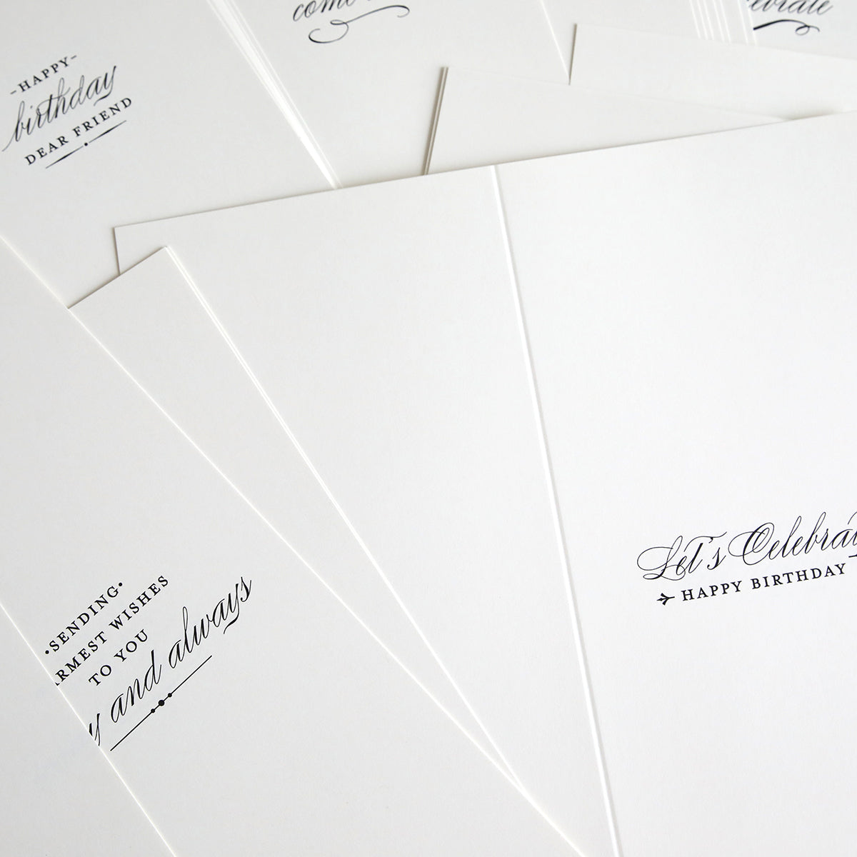 A close-up of Slimline Birthday Card Sentiment Inserts: several white cards with black cursive text and elegant ivory inserts, partially overlapping on a flat surface.