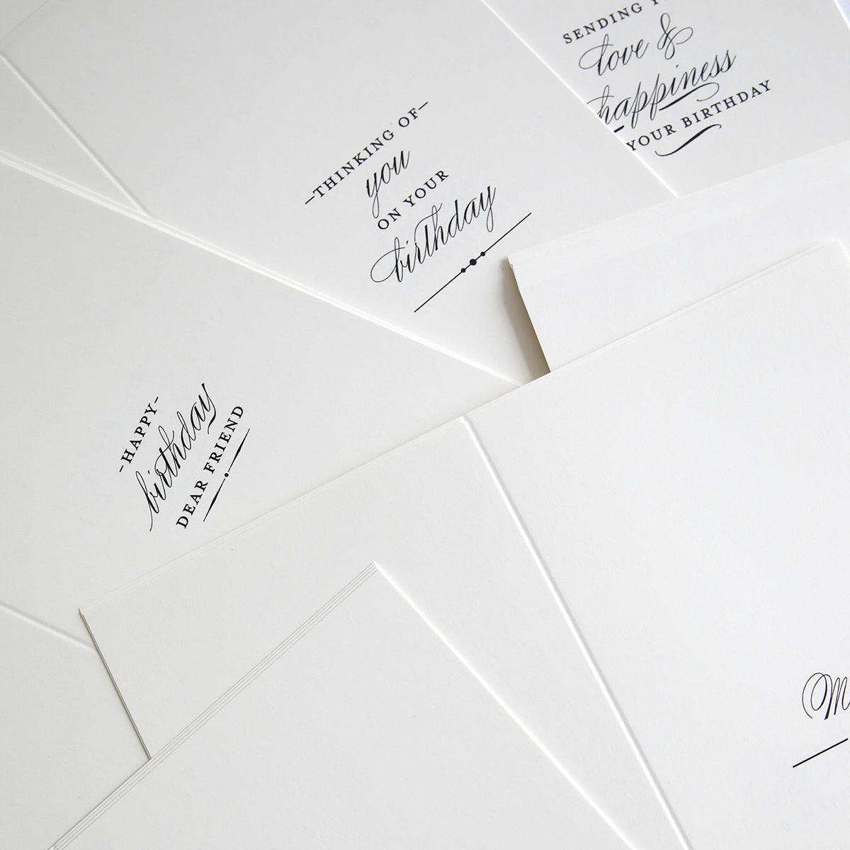 Slimline Birthday Card Sentiment Inserts are arranged on a flat surface, featuring several white cards with minimalist black text for birthdays and general well wishes.
