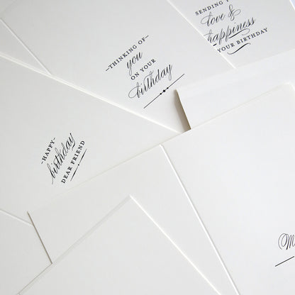 Slimline Birthday Card Sentiment Inserts are arranged on a flat surface, featuring several white cards with minimalist black text for birthdays and general well wishes.