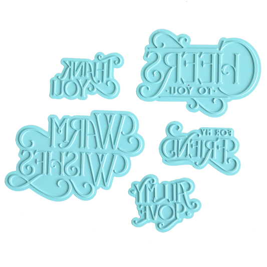 Five light blue Gilded Essential Sentiments Foil Plates featuring reversed text with phrases such as “CHEERS TO YOU!” and “THANK YOU” are displayed on a white background—ideal for adding unique touches to handmade cards or elevating your next paper crafting project.