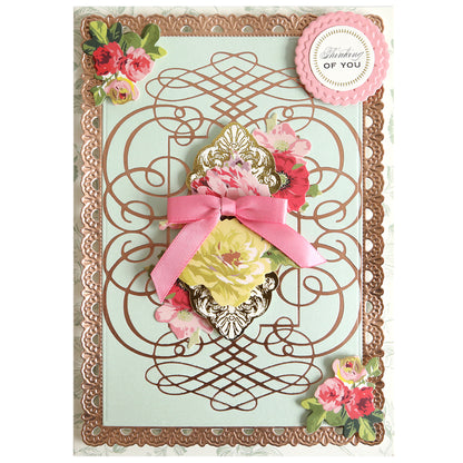 A decorative greeting card featuring elegant floral designs, intricate gold accents created with the Calligraphy Frame Gilded Hot Foil Plate, a pink ribbon embellishment, and a round “Thinking of You” label positioned in the top right corner.