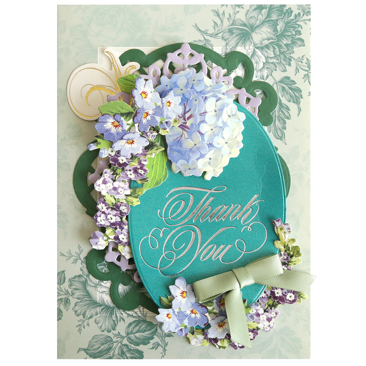 Thoughtful Calligraphy Gilded Hot Foil Plates create an oval teal plaque with gold-foiled “Thank You” text, accented by purple and blue florals and a sage green ribbon, on a light green background.