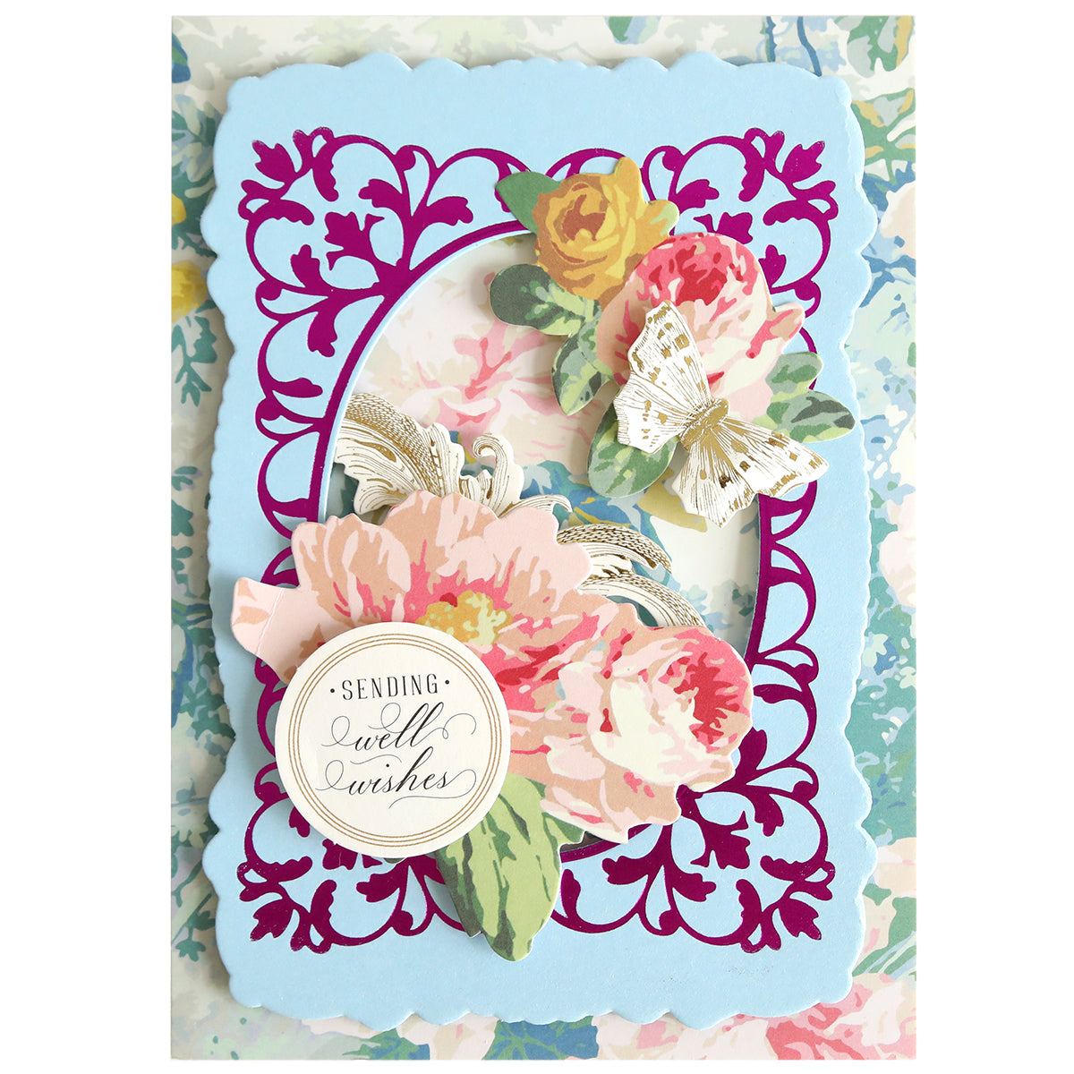 Decorative handmade card featuring the Oval Flourish Frame Gilded Hot Foil Plate with intricate floral cut-out details, layered pink and yellow flowers, a butterfly, and a round label reading “Sending Well Wishes.” The pastel floral patterned background adds an elegant touch, making it perfect for your handmade cards.