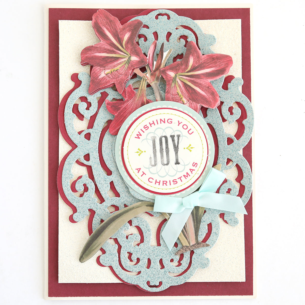 Handmade Christmas card featuring red flowers, an ornate blue frame, and a round “Wishing You Joy at Christmas” tag tied with a blue ribbon on a red and cream background. Beautifully finished with 3D greeting card accents using the Favorite Christmas Sentiment Stickers for an extra festive touch.