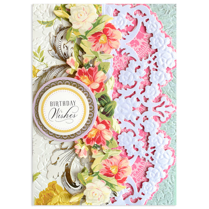 A decorative birthday card with floral designs, ornate white lace patterns made using Opulent Border Cut and Emboss Dies, and a circular label reading "Birthday Wishes.