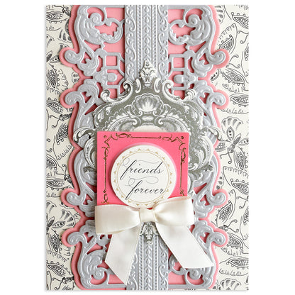 A decorative greeting card featuring ornate silver and pink designs created with Opulent Border Cut and Emboss Dies, elegant embellishments, a white ribbon bow, and a round "friends forever" label on a patterned background.