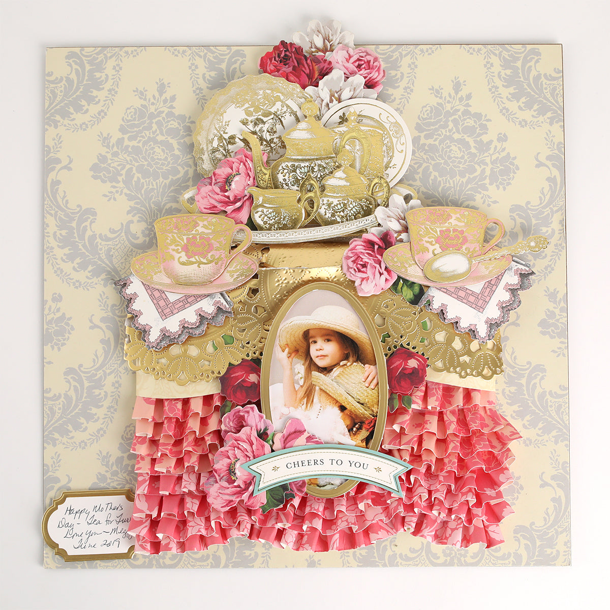 A decorative collage features teapots, teacups, pink flowers, ruffled paper, and a framed photo of a child in a hat, all adorned with accents from the Favorite Tea Embellishments 120 Count. A “Cheers to You” banner and a handwritten note in the bottom left corner complete this charming handmade card.