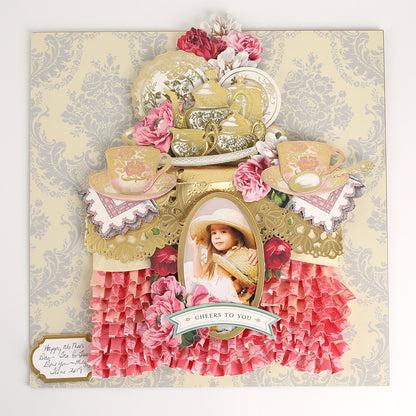 A decorative collage features teapots, teacups, pink flowers, ruffled paper, and a framed photo of a child in a hat, all adorned with accents from the Favorite Tea Embellishments 120 Count. A “Cheers to You” banner and a handwritten note in the bottom left corner complete this charming handmade card.
